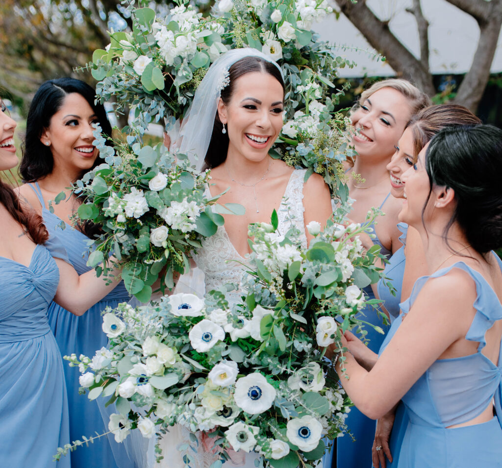 A beautiful bride surrounded by her bridesmaids, each holding vibrant flowers close to her. 