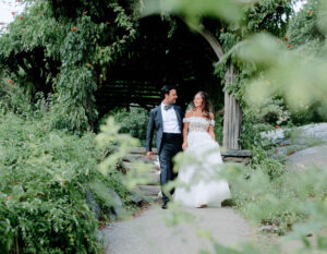 A bride and groom walking hand in hand through the scenic beauty of Central Park on their wedding day.