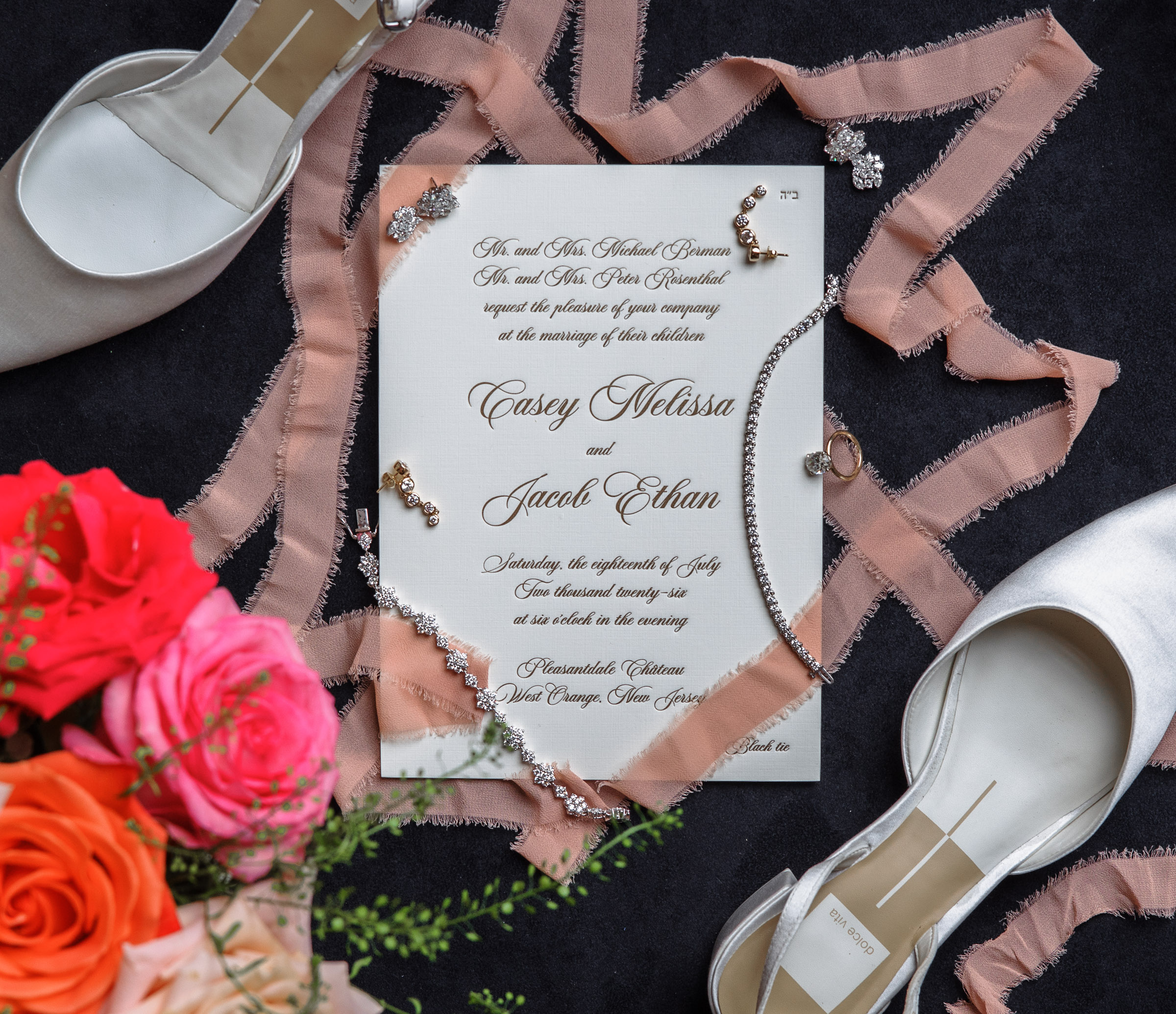 Casey and Jacob’s black-tie wedding invitation with jewelry, shoes, ribbon, and coral flowers