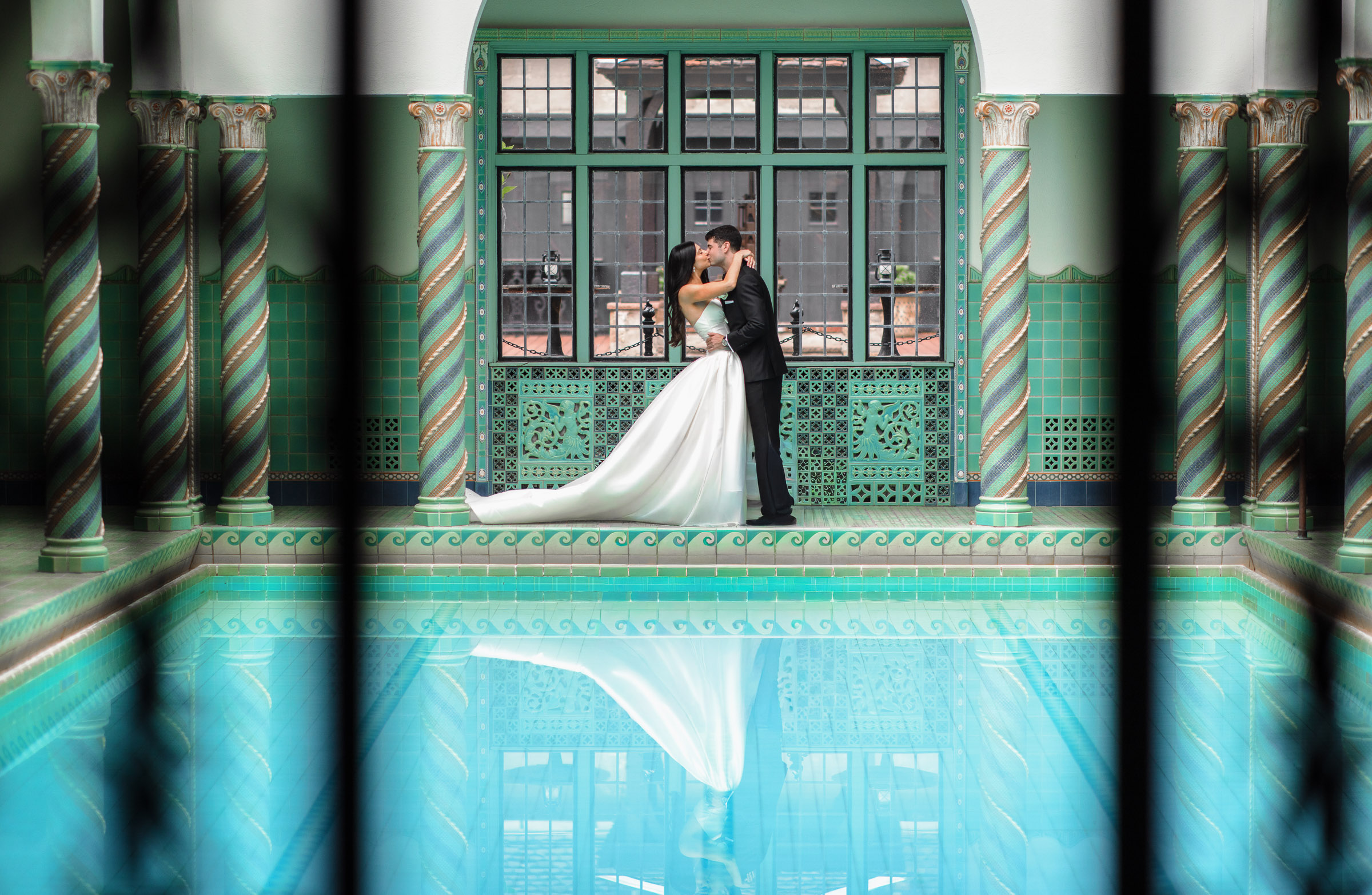 Casey and Jacob beside the turquoise tile and windows of the indoor pool