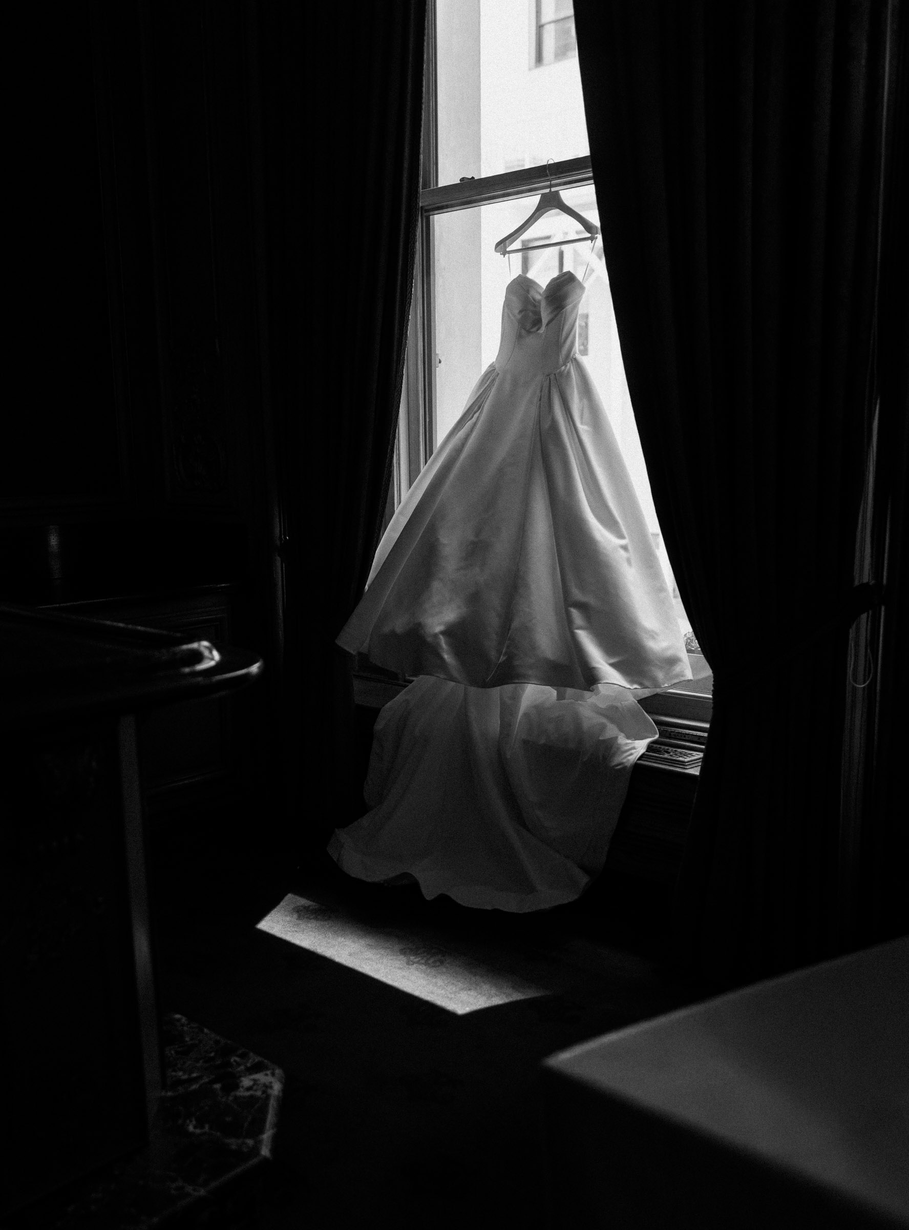 Wedding dress hanging in window light before the ceremony