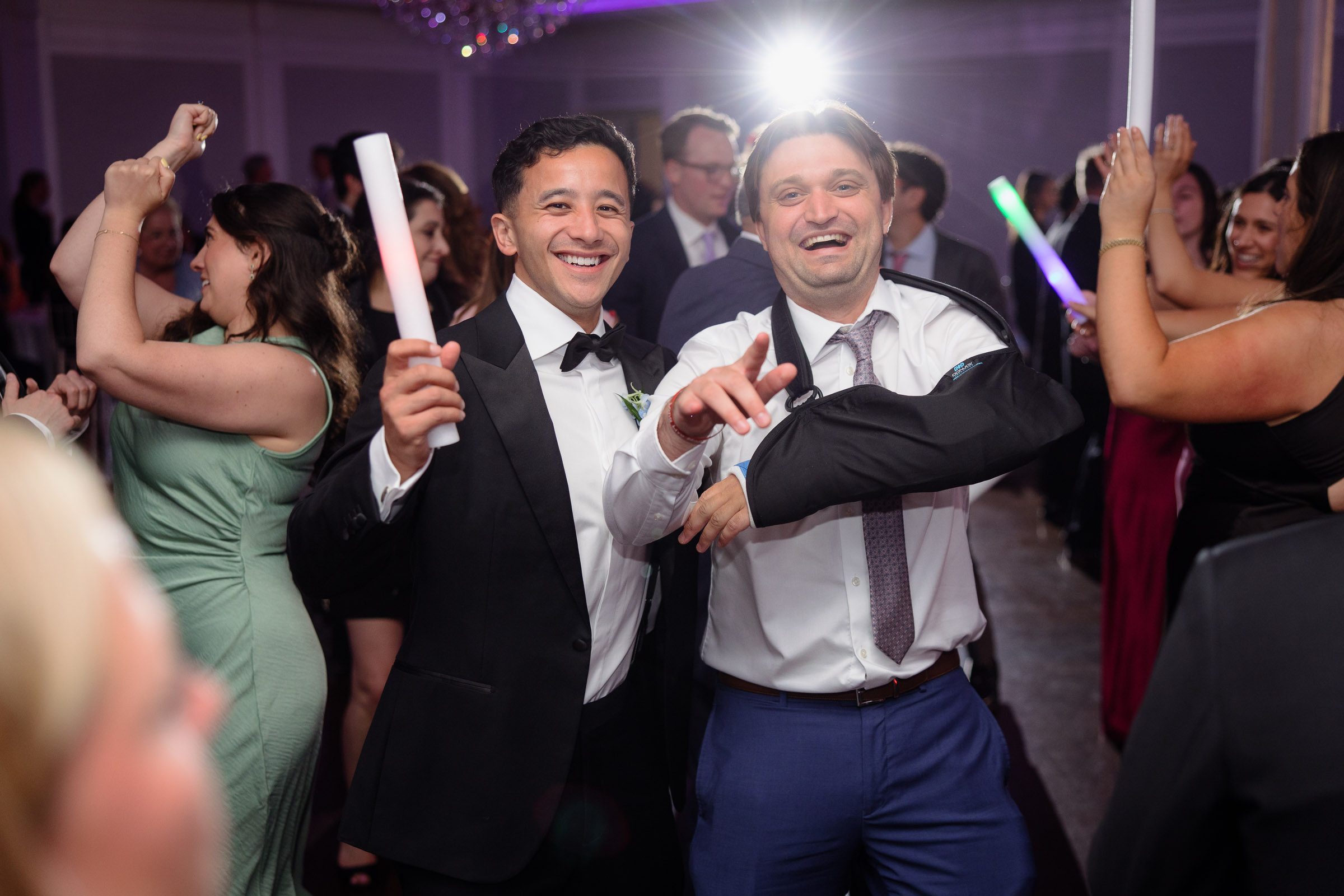 Guests dancing with glow sticks under colorful ballroom lights