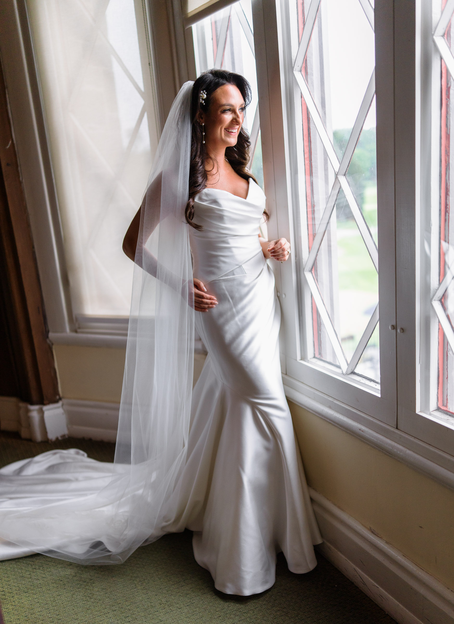Alexandra in her satin wedding gown beside a tall window at Whitby Castle