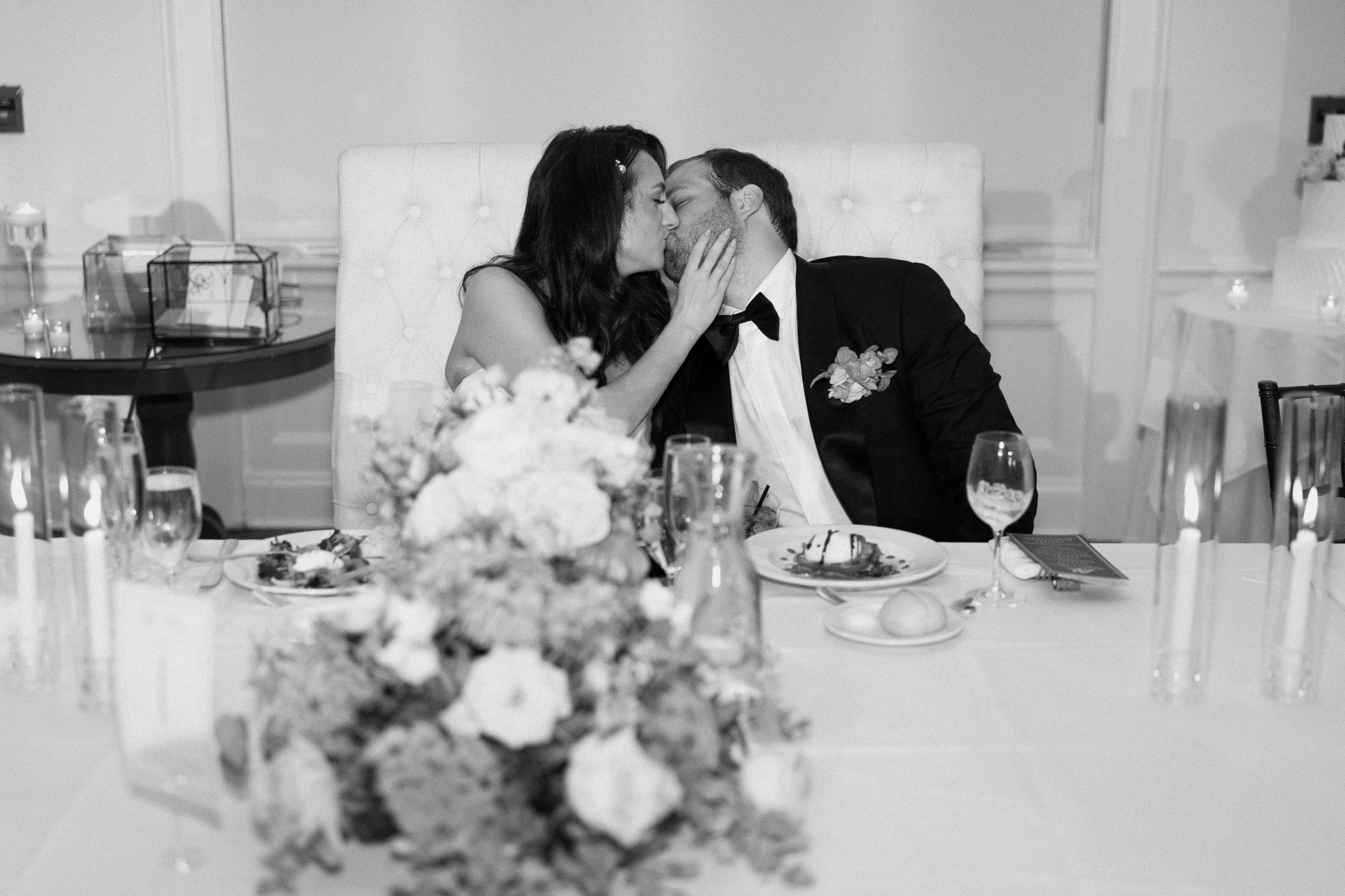 Alexandra and Ryan sharing a black-and-white kiss at their sweetheart table