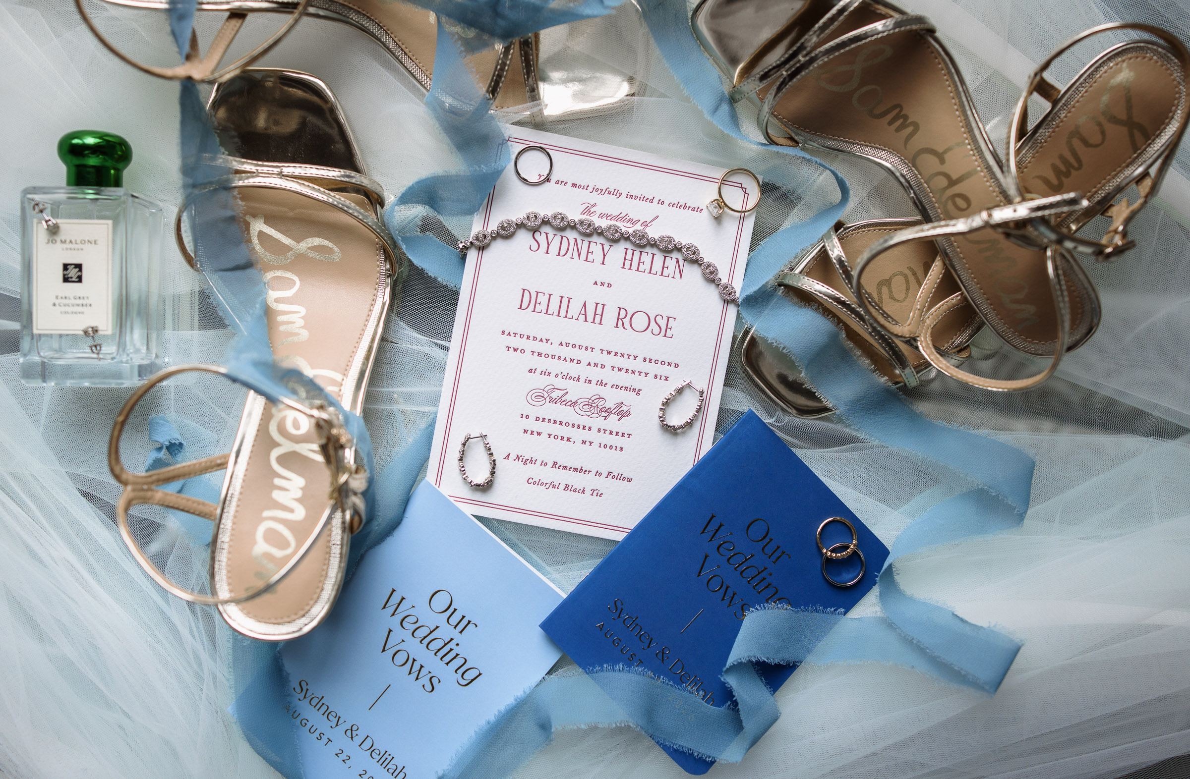 Sydney and Delilah’s wedding invitation styled with both pairs of shoes, rings, perfume, and blue vow books