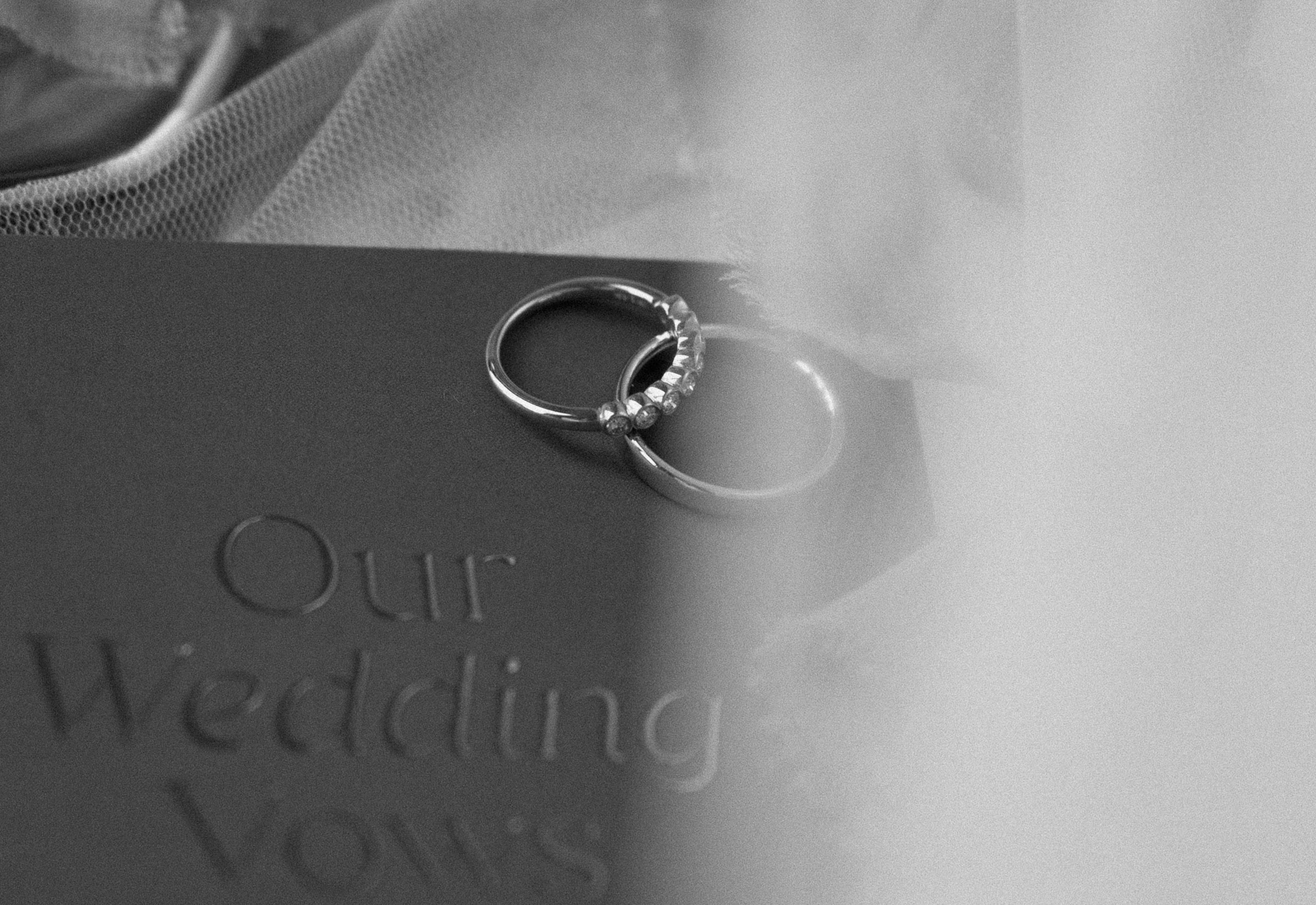 Wedding rings resting on a blue vow book in a black-and-white detail photograph