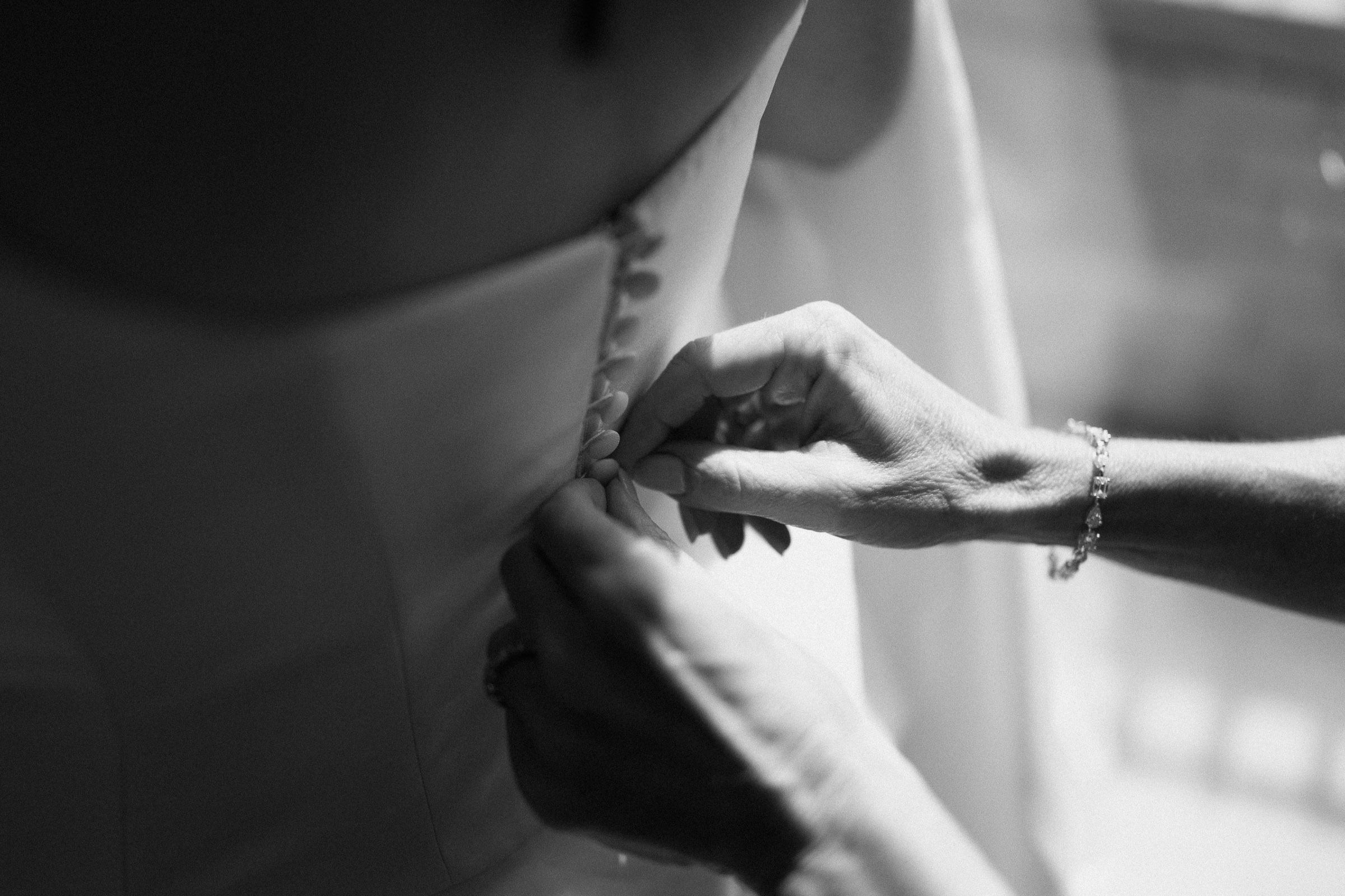 A close black-and-white moment as a loved one helps fasten the back of a wedding gown