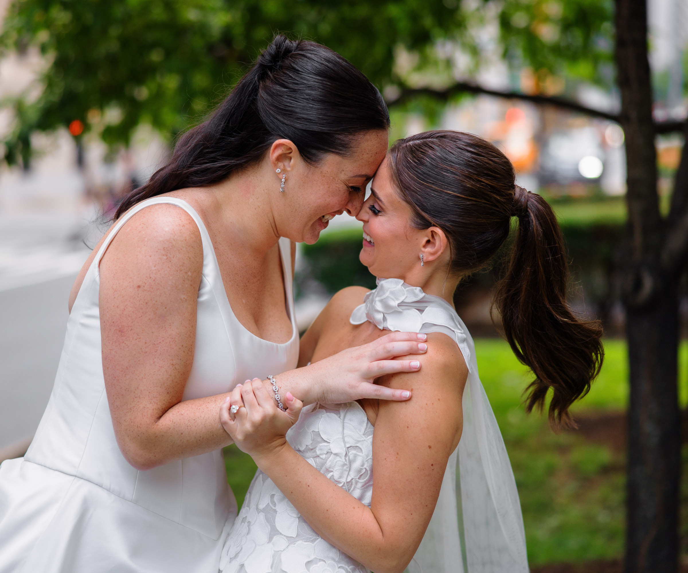 The brides holding each other beneath the trees during city portraits