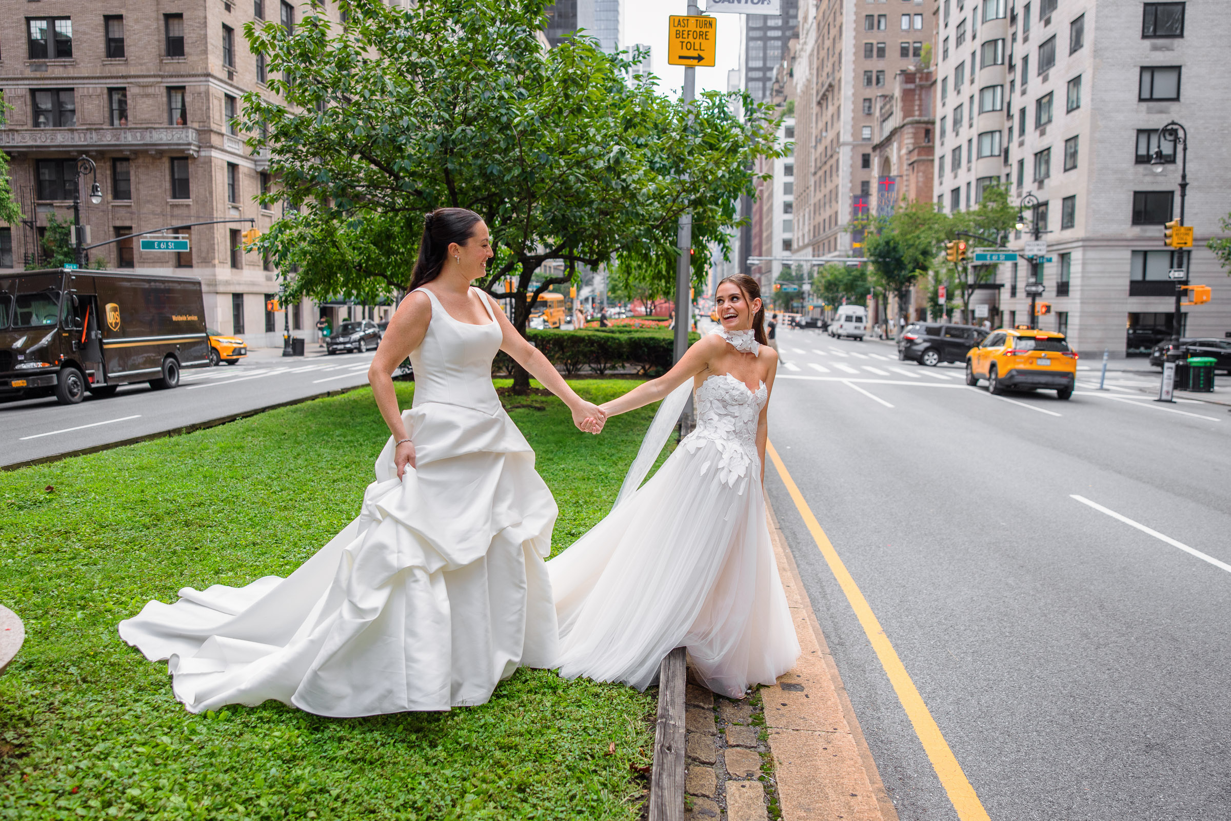 Sydney and Delilah walking hand in hand through a green median with yellow taxis behind them