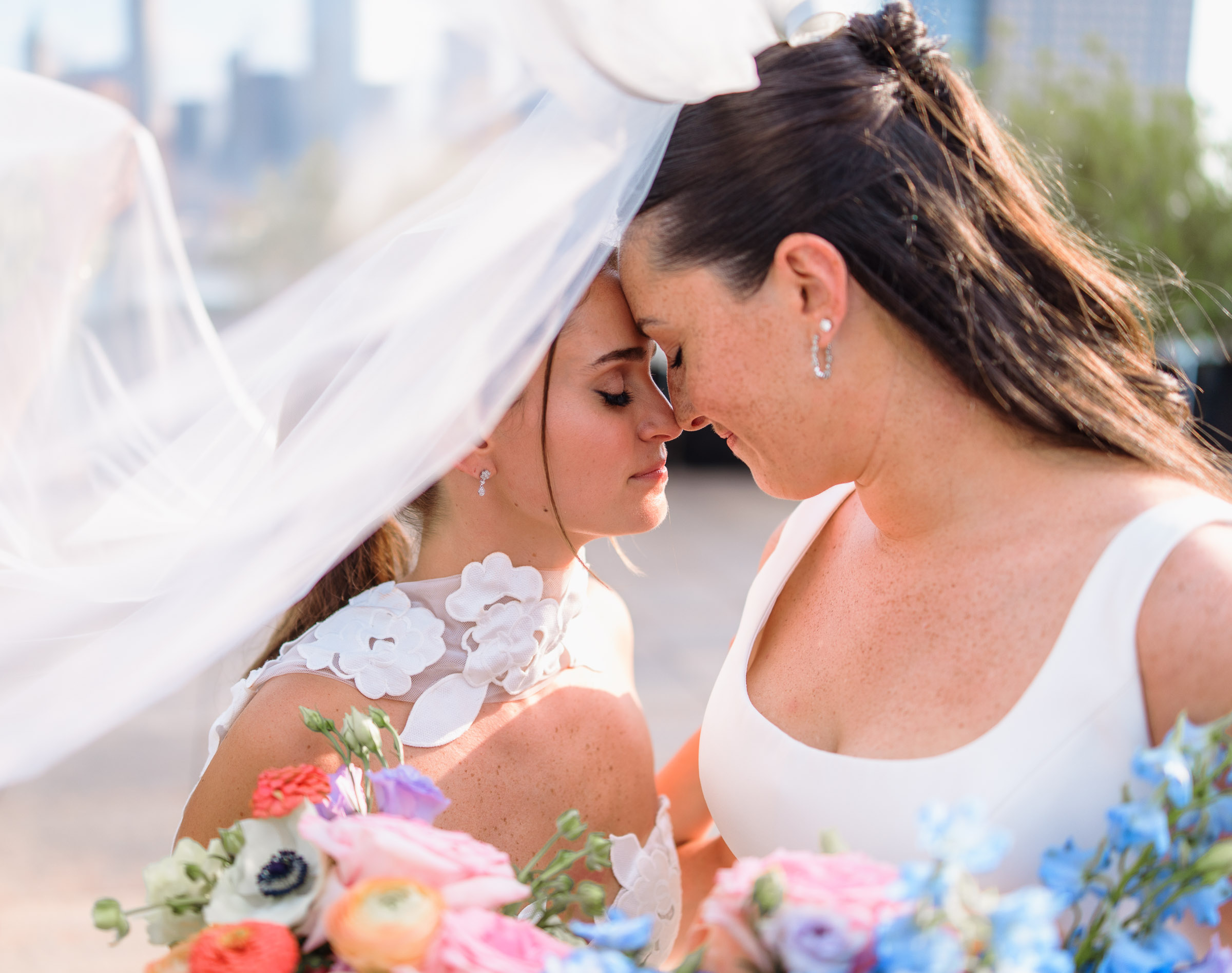 Sydney and Delilah touching foreheads beneath a veil with colorful bouquets in the foreground