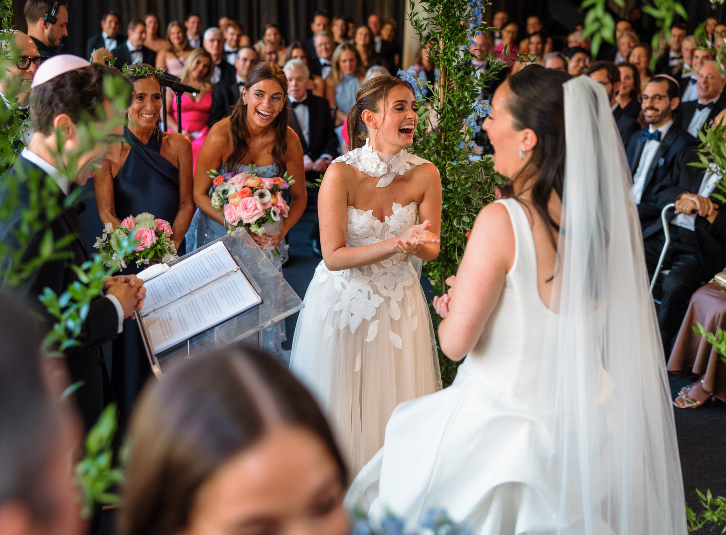 Sydney and Delilah laughing during their indoor wedding ceremony as guests look on