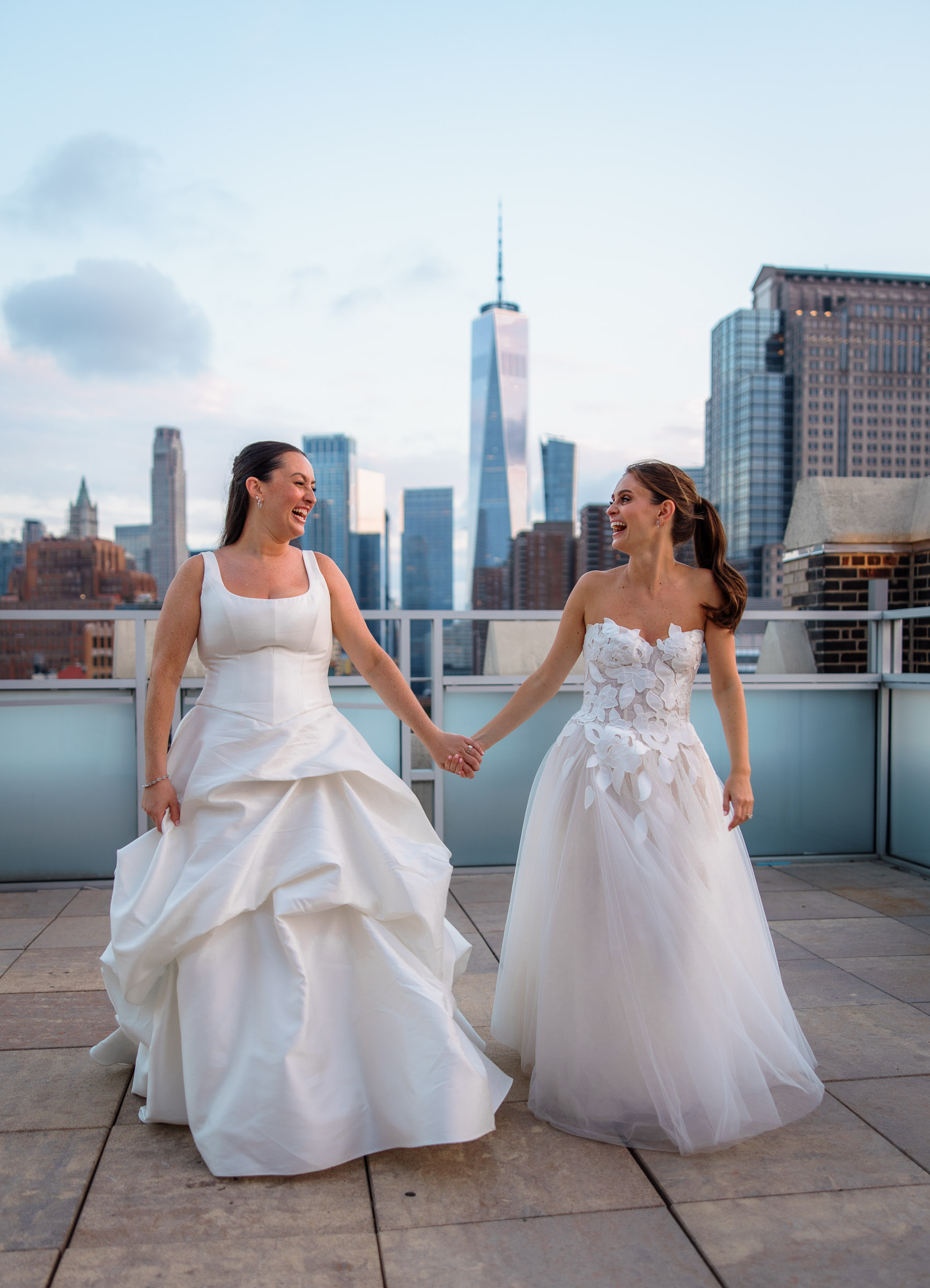 The brides walking hand in hand across the rooftop with the downtown skyline ahead