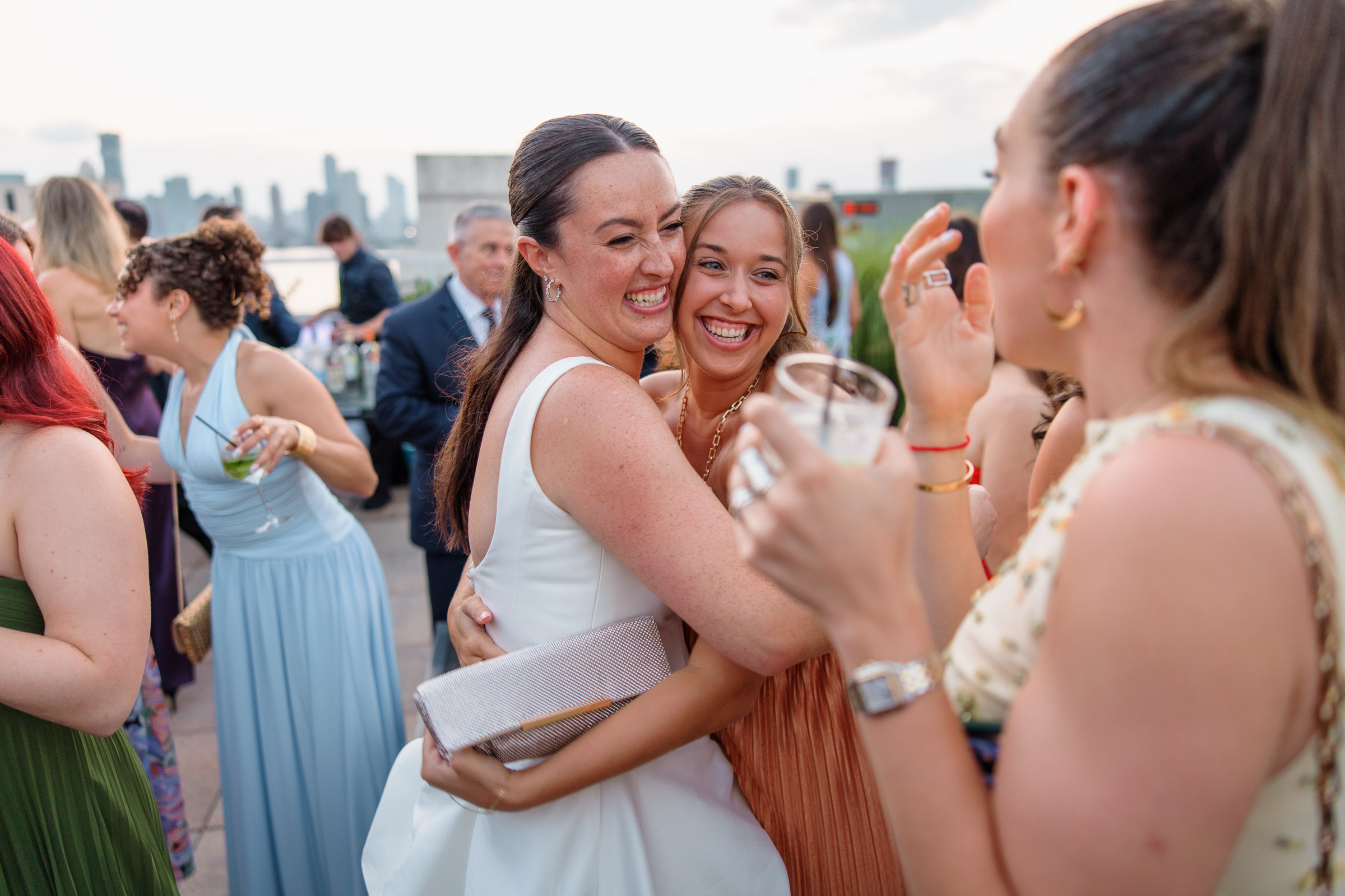 The brides laughing with a guest during cocktail hour on the Tribeca Rooftop terrace