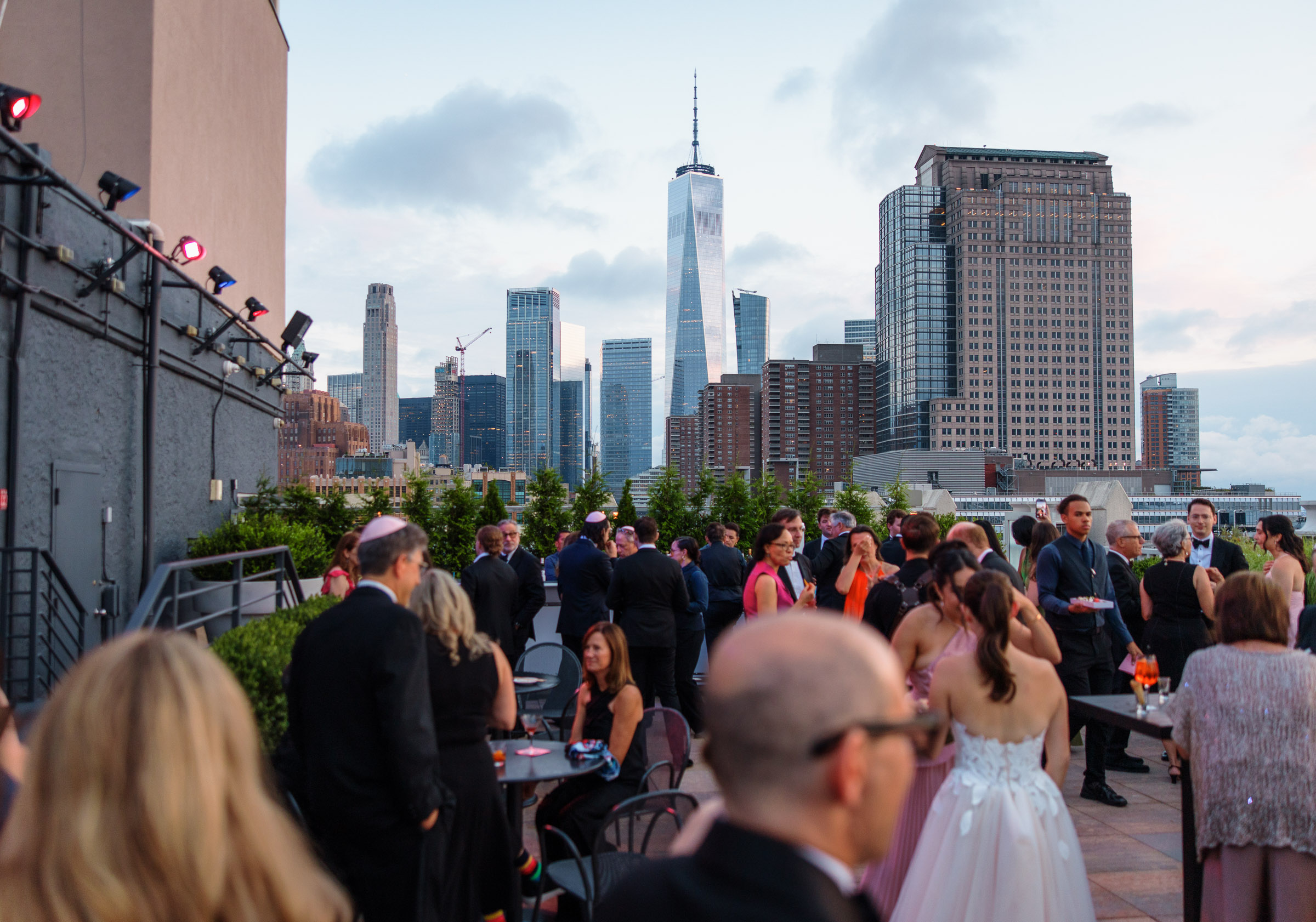 Wide view of wedding guests mingling at rooftop cocktail hour with the Lower Manhattan skyline