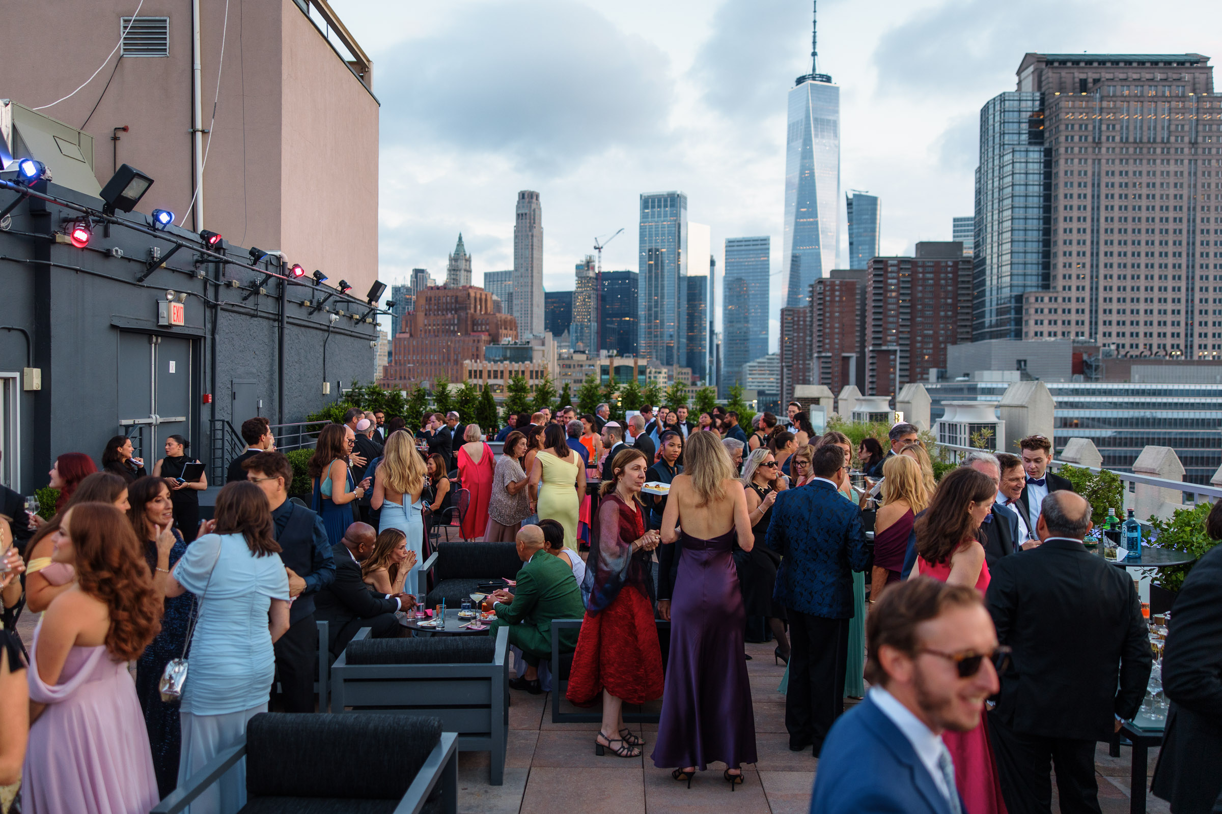 Wedding guests gathering across the rooftop terrace during cocktail hour with the downtown skyline behind them