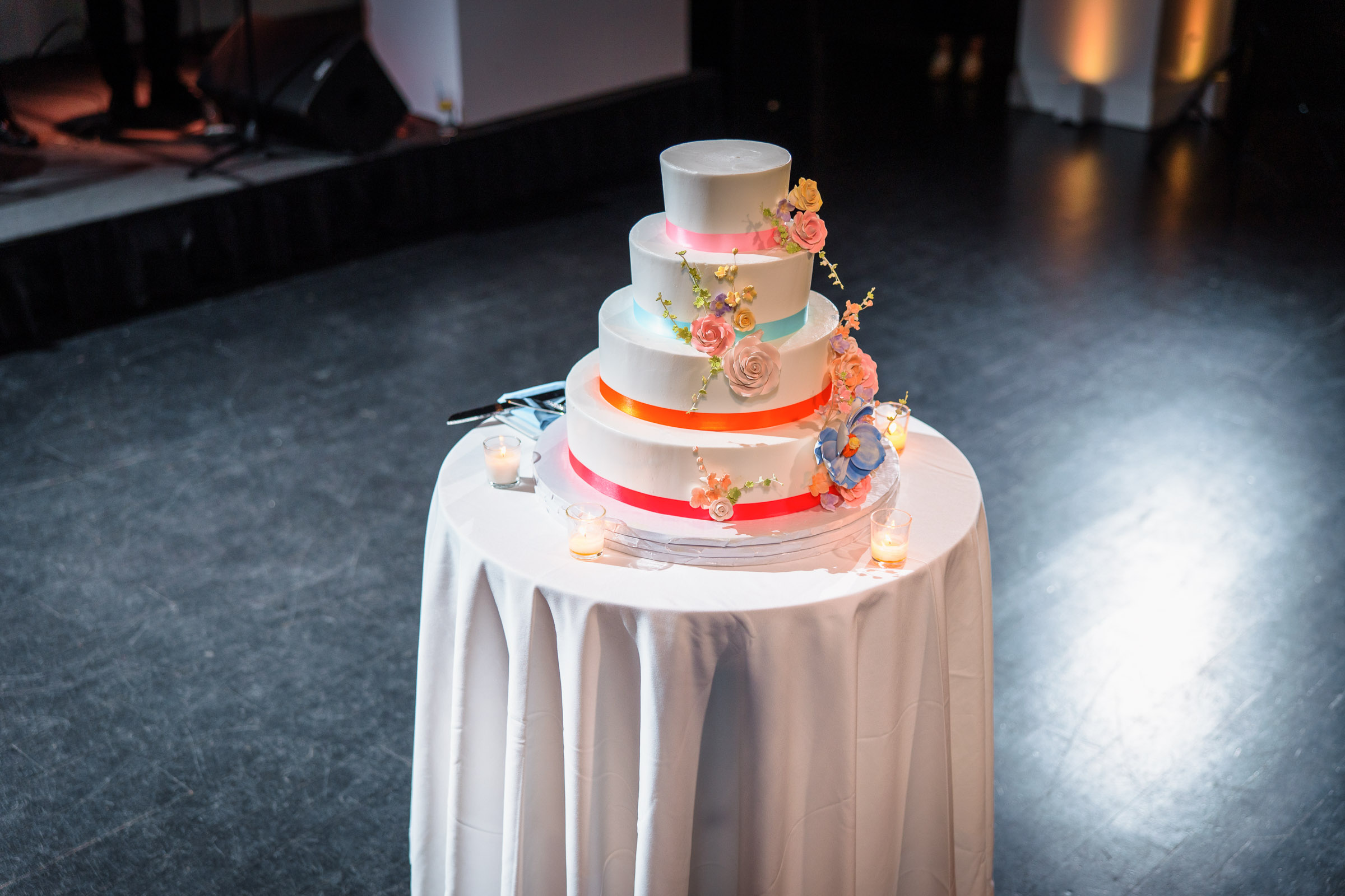 Three-tier wedding cake decorated with colorful flowers and ribbon details